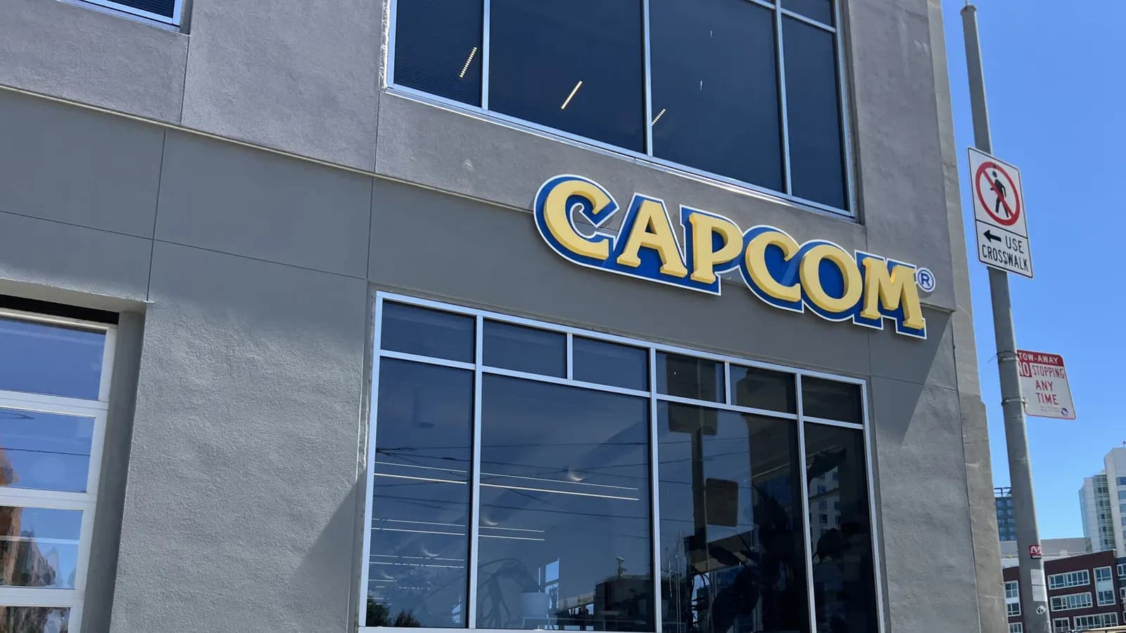 Capcom building facade with the yellow-and-blue Capcom logo above glass windows, with traffic signs beside it