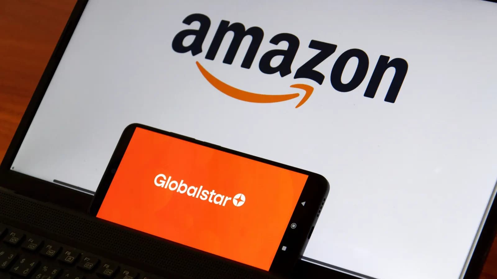 Smartphone displaying the Globalstar logo in front of a laptop screen showing the Amazon logo