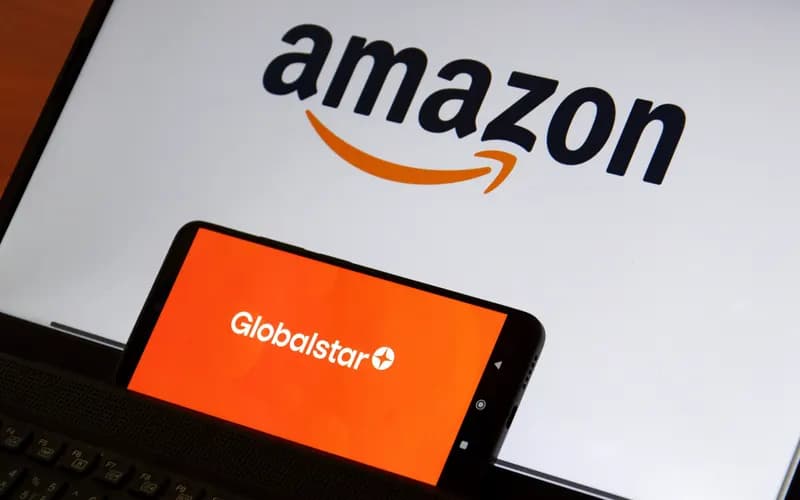 Smartphone displaying the Globalstar logo in front of a laptop screen showing the Amazon logo