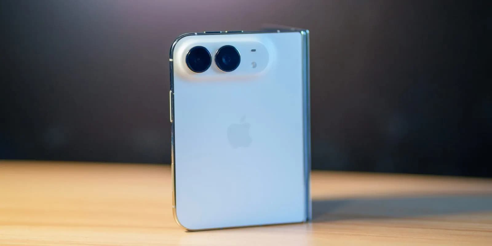 Light blue foldable Apple phone with dual rear cameras standing upright on a wooden table