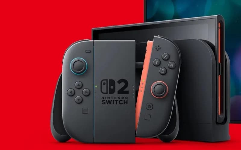 Nintendo Switch 2 console with gray and orange Joy-Con controllers beside its docking station on a red background
