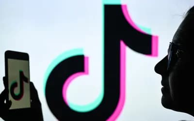 Silhouette of a woman in glasses holding a phone, with the TikTok logo on its screen and a giant screen behind her