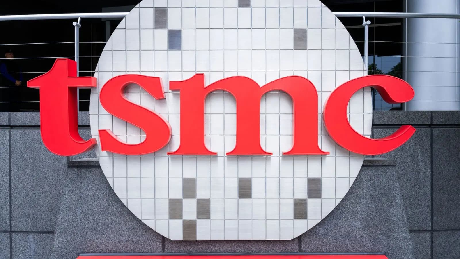 Red TSMC logo on a round white-tiled panel shaped like a chip wafer, mounted on a building's granite wall