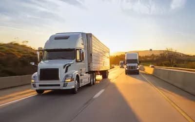 White semi-truck driving down a highway at sunset, with other trucks approaching from the opposite direction