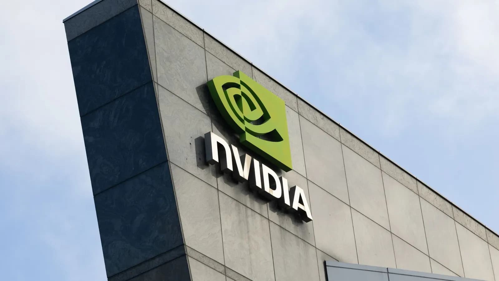 Mavi gökyüzü altında, gri ve koyu cepheli bir binanın üzerinde yer alan yeşil Nvidia logosu ve yazısı