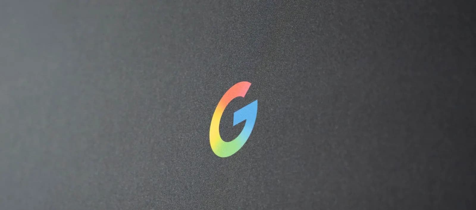 Google's colorful gradient "G" logo on a dark gray matte surface
