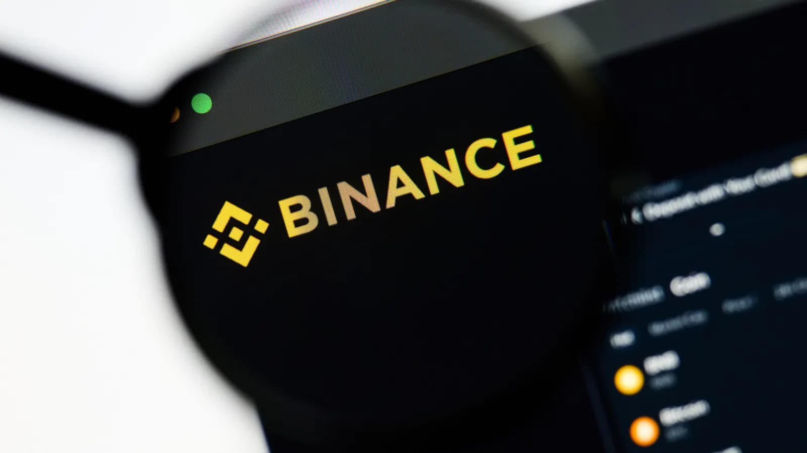 Büyüteç altında Binance kripto para borsası web sitesinin logosu ve koyu temalı ekran görünümü