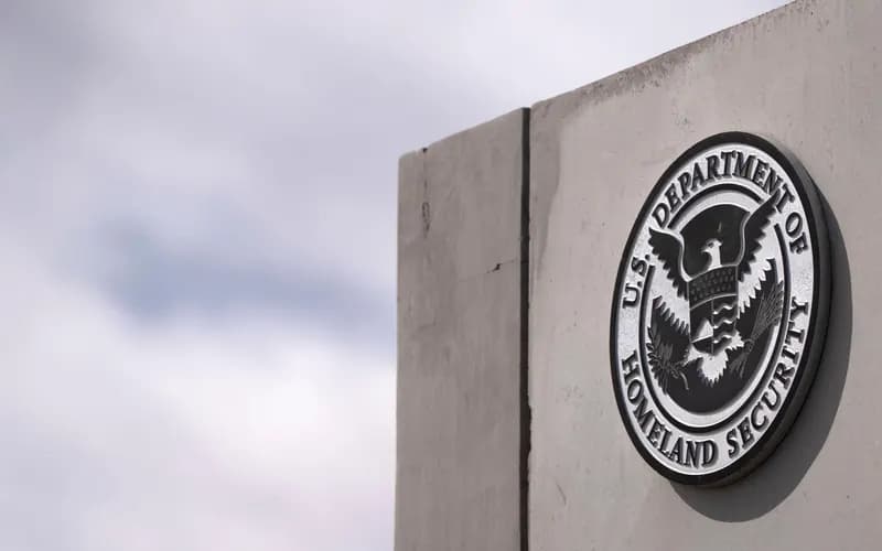 U.S. Department of Homeland Security seal mounted on a gray concrete wall, with a cloudy sky in the background