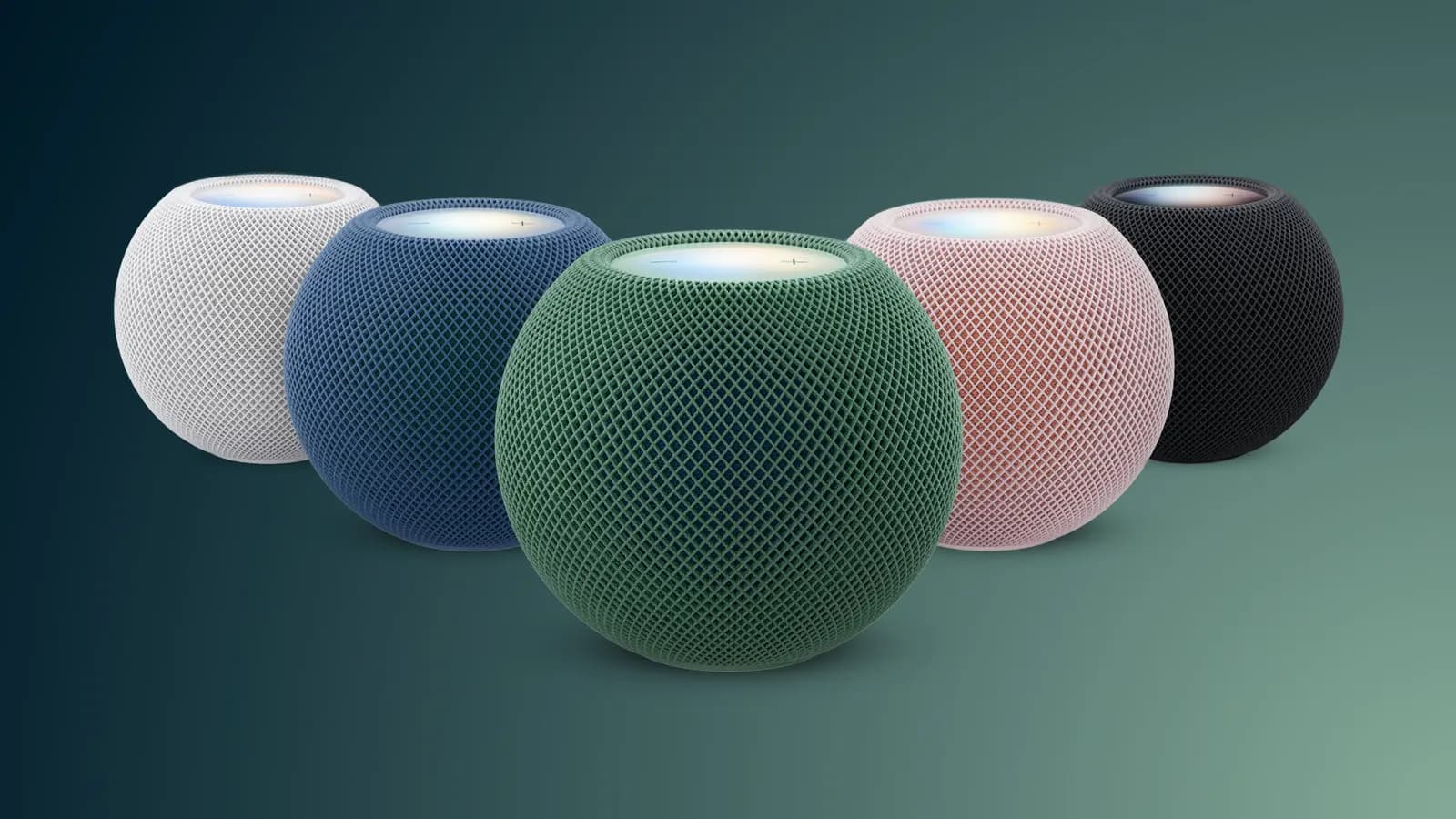 Five small smart speakers in white, blue, green, pink, and black stand side by side on a green background.
