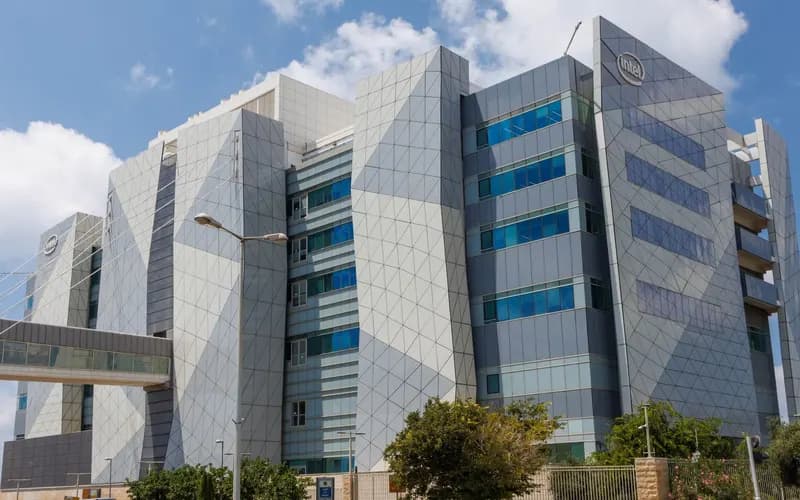 Modern office building with gray geometric cladding and an Intel logo on its facade, with a glass walkway under a blue sky