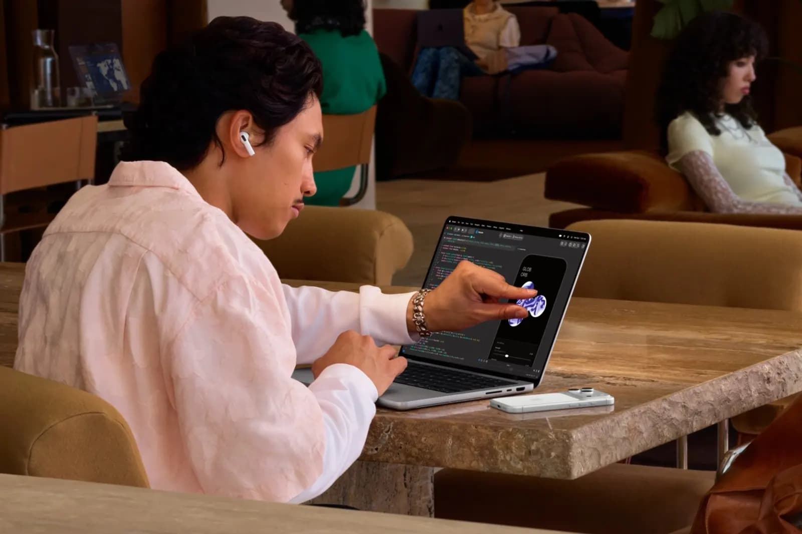Man wearing headphones touches a laptop screen in a café, using an app that shows code and visuals.