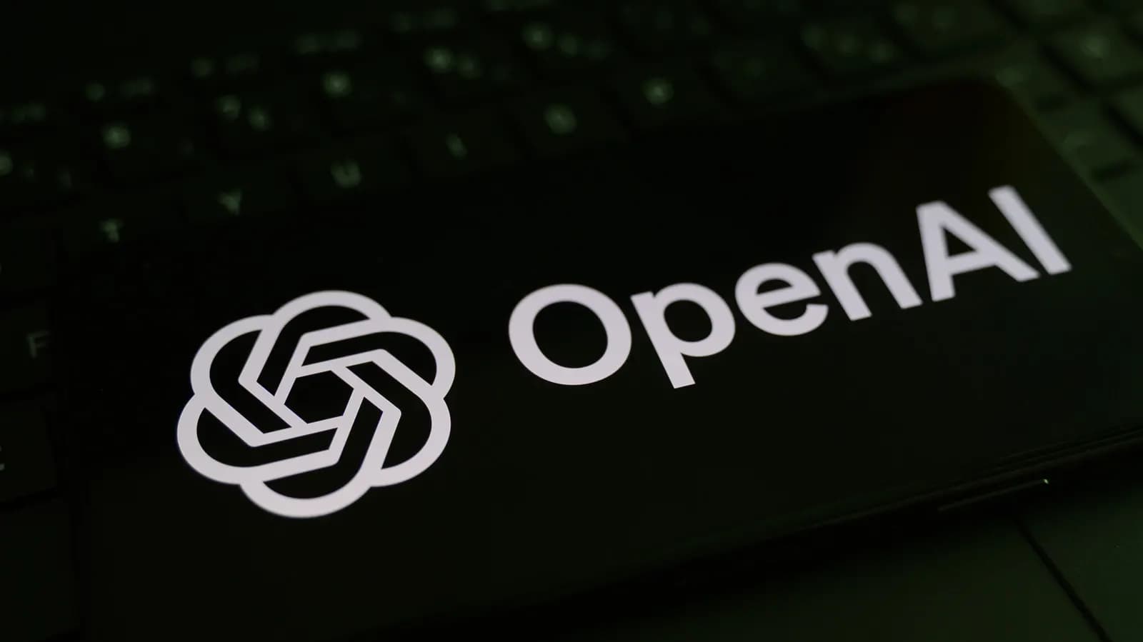 Klavyenin üzerinde duran, ekranında OpenAI logosu ve yazısı görünen siyah telefon