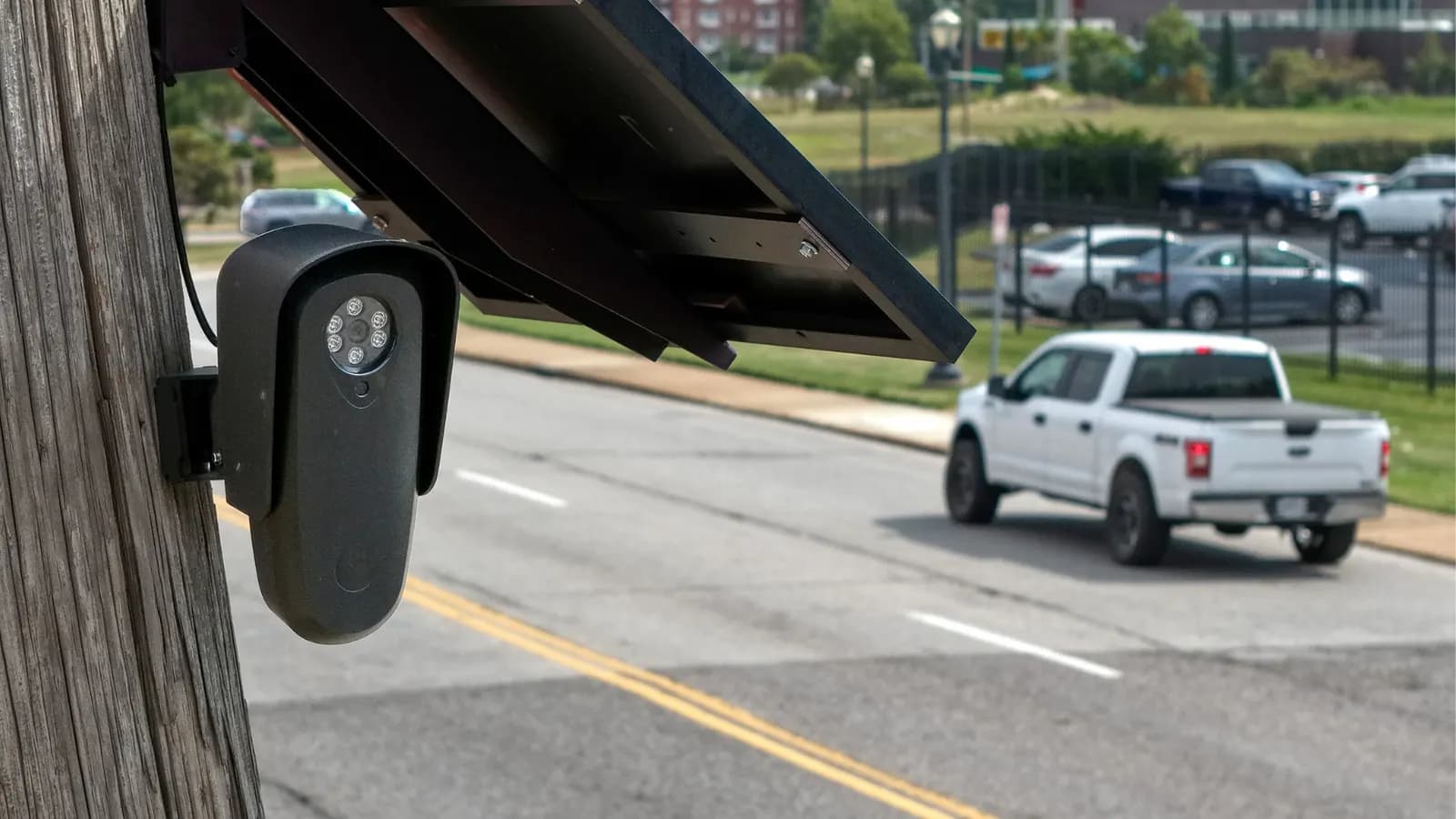 Solar-powered security camera mounted on a pole, with a white pickup truck driving down the street in the background
