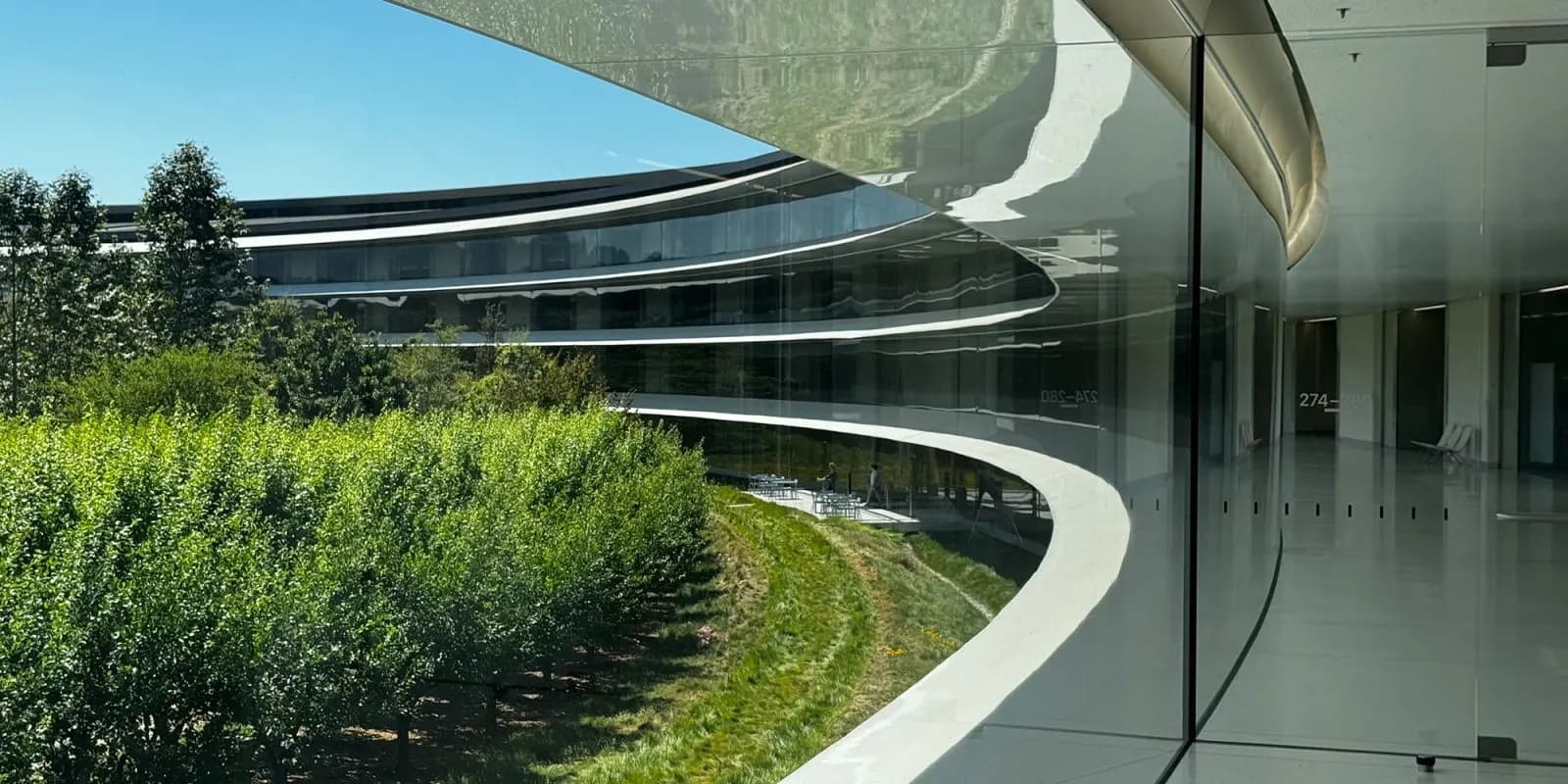 Circular office building with a curved glass facade on a sunny day, with a green orchard and lawn in front