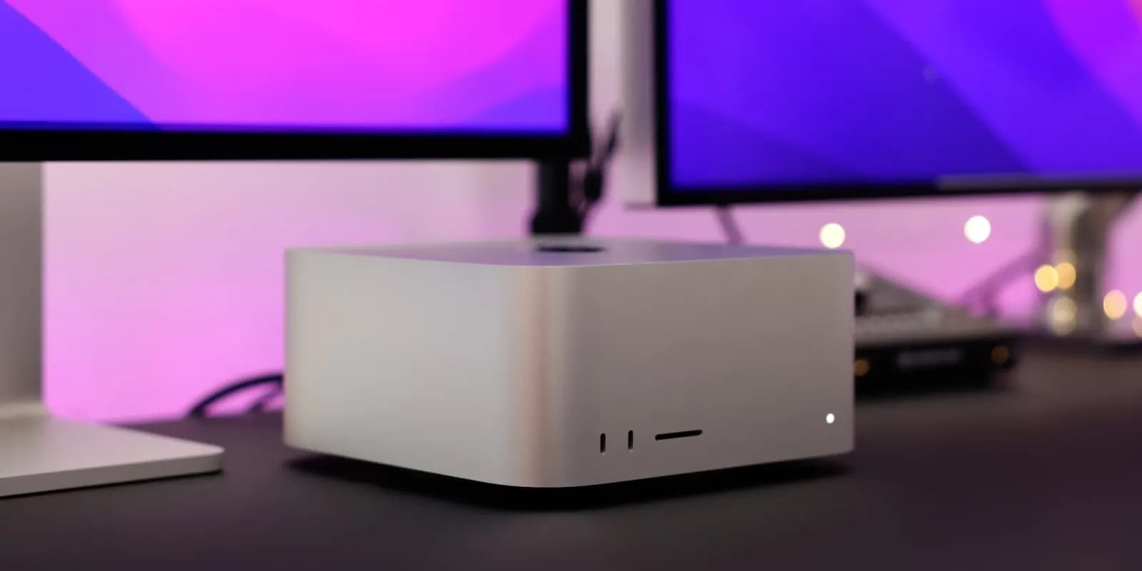 Silver Mac Studio on a desk in front of two monitors with purple backgrounds