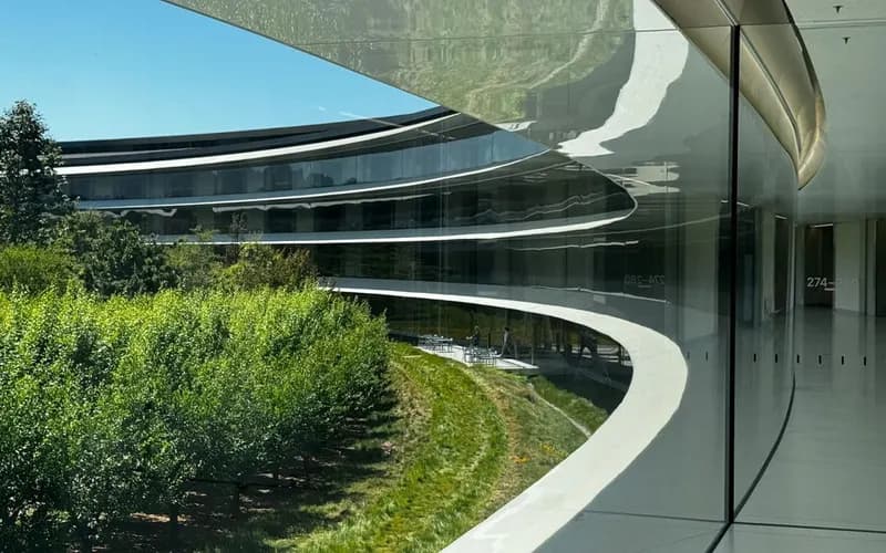 Circular office building with a curved glass facade on a sunny day, with a green orchard and lawn in front