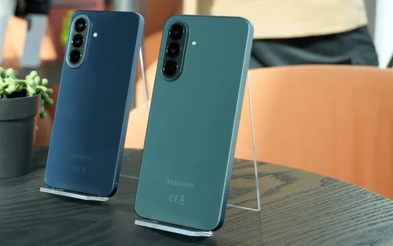 Back of two blue and green Samsung smartphones standing on acrylic stands on a black table
