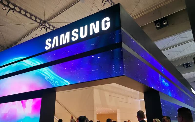 Large Samsung booth with glowing logo, ringed by purple and blue LED screens, as visitors browse the trade show floor below