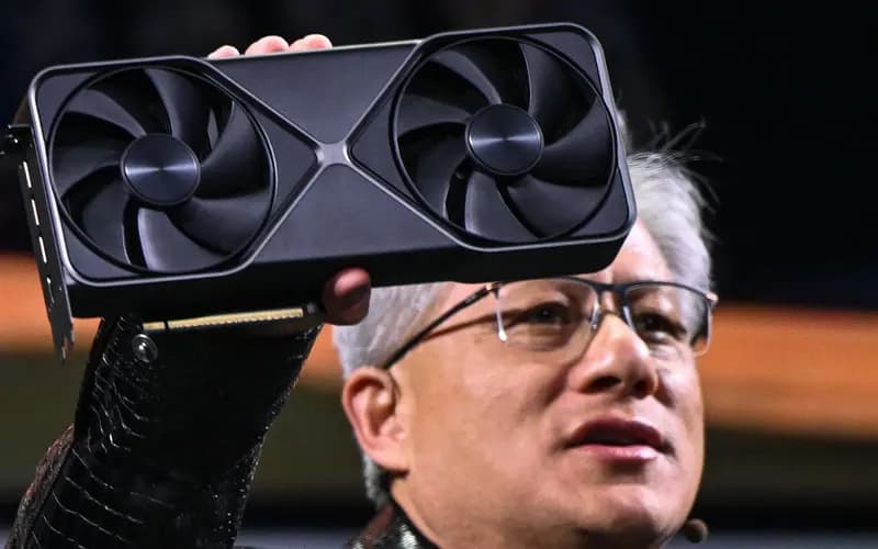 A gray-haired man in glasses holds up a black dual-fan graphics card on stage.