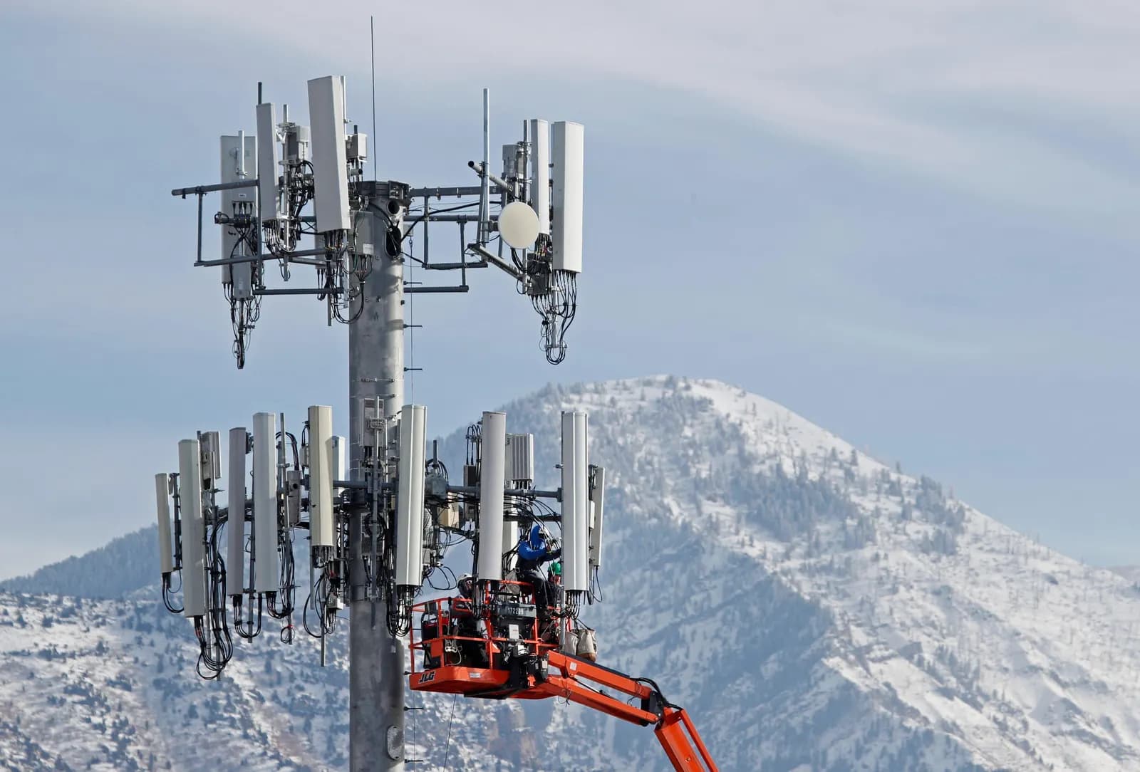 Karlı dağların önünde, hücresel kulenin antenlerinde vinç sepetiyle çalışan teknisyenler