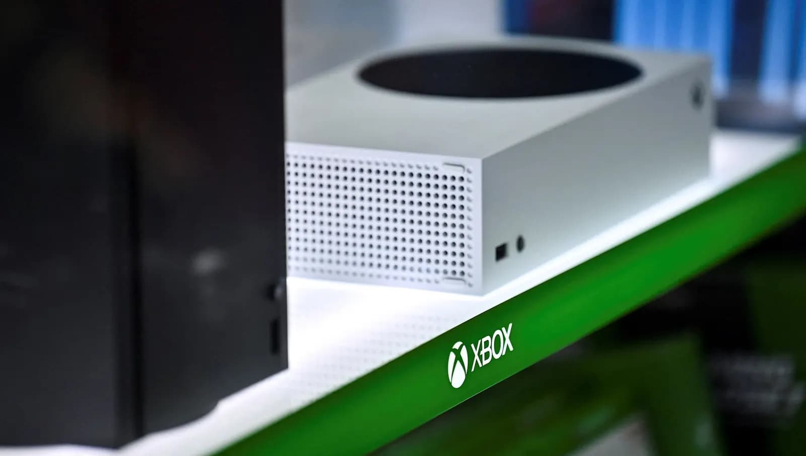 White Xbox Series S and black Xbox Series X consoles side by side on a store shelf with a green Xbox logo edge