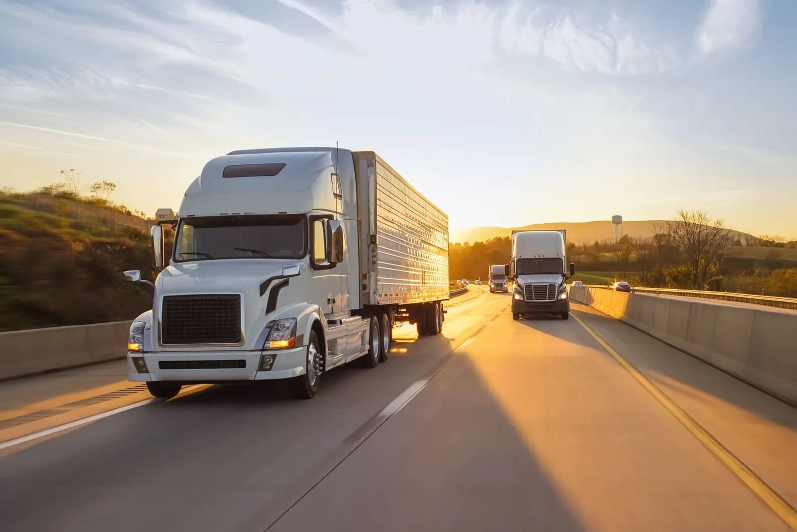 White semi-truck driving down a highway at sunset, with other trucks approaching from the opposite direction
