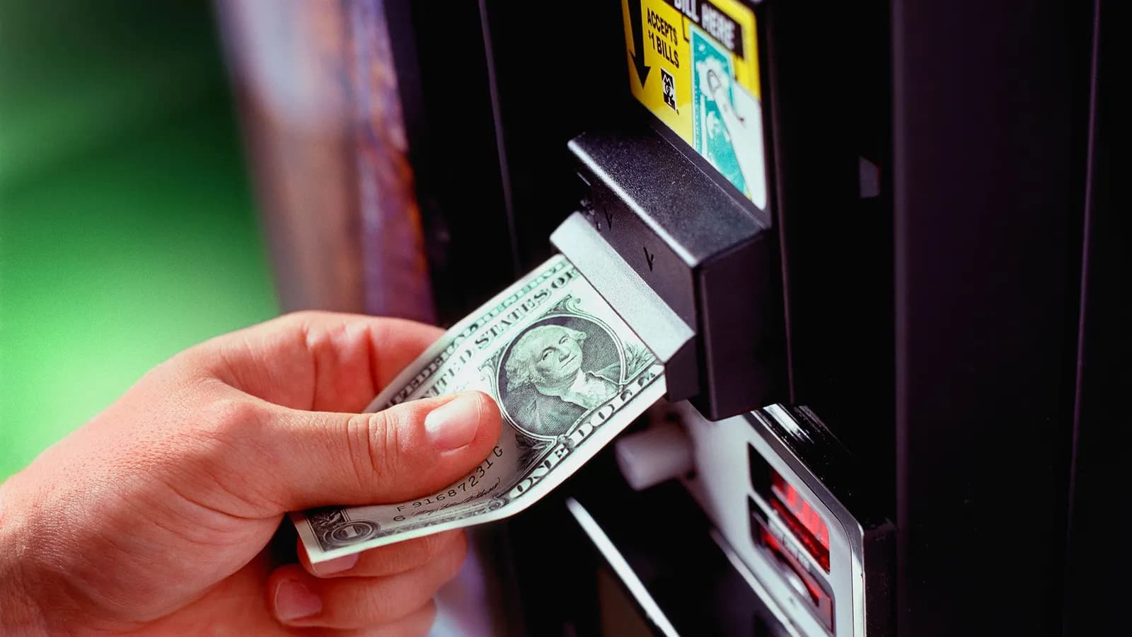 Bir el, otomat makinesinin banknot okuyucusuna bir dolarlık banknotu sokuyor.